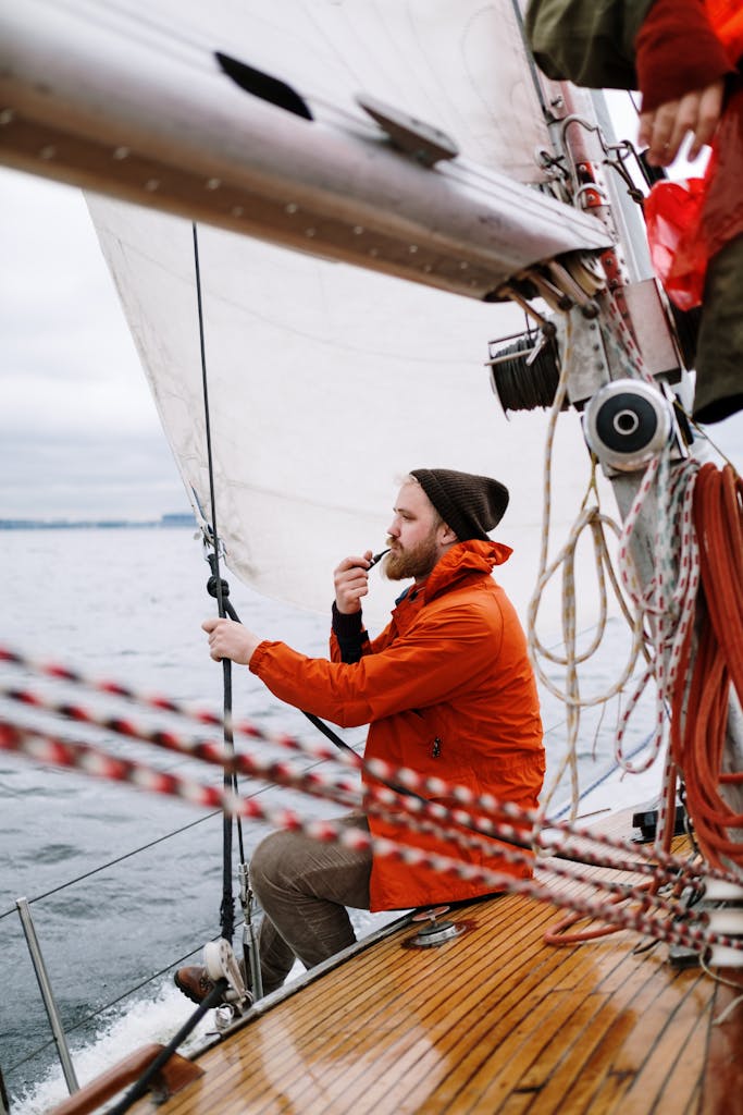 Man in Orange Jacket Holding a Tabaco Pipe While Sitting on the Boat